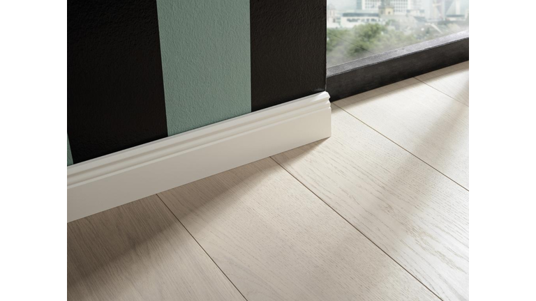 Sockelleiste weiß foliert, profiliert und schließt an gestreifte Wand und hellem Holzboden an.